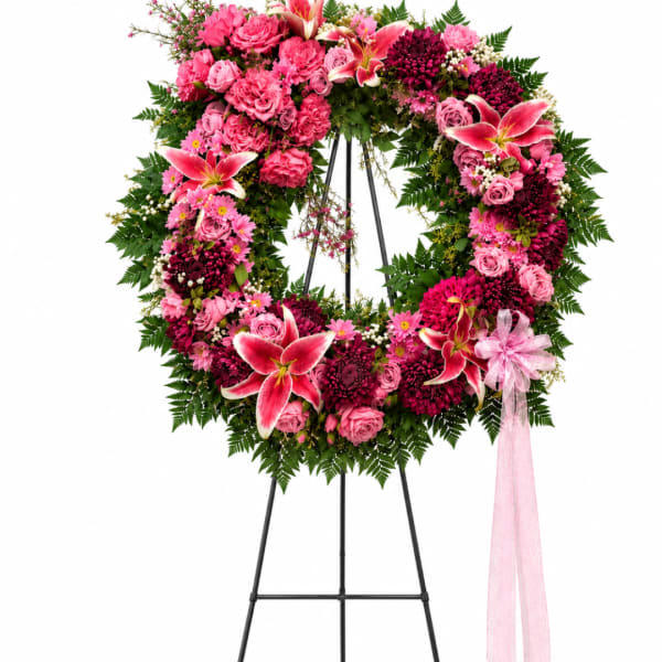 Pink and burgundy floral wreath on a black stand with a pink ribbon