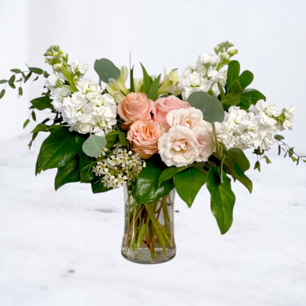 Pink and white roses in a clear glass vase with greenery