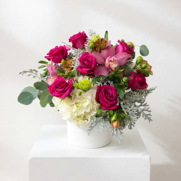 Pink roses and orchids arranged in a white vase.