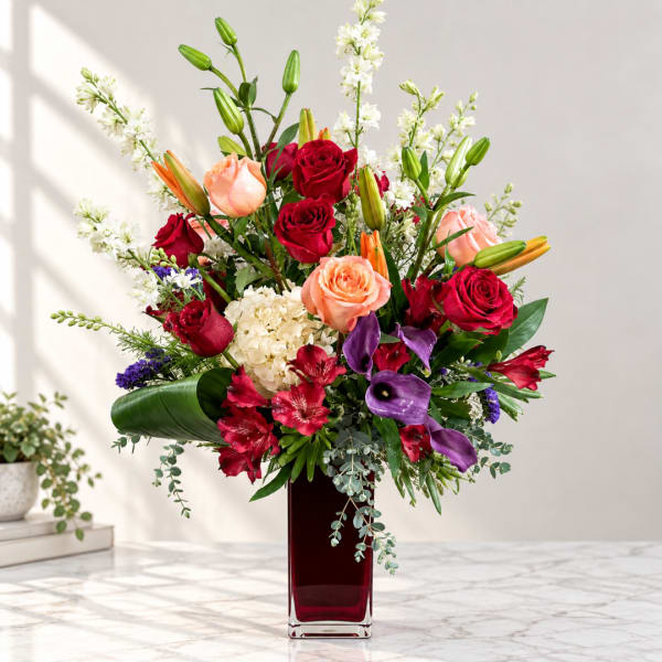Mixed bouquet of roses, lilies, and purple calla lilies in a tall red vase