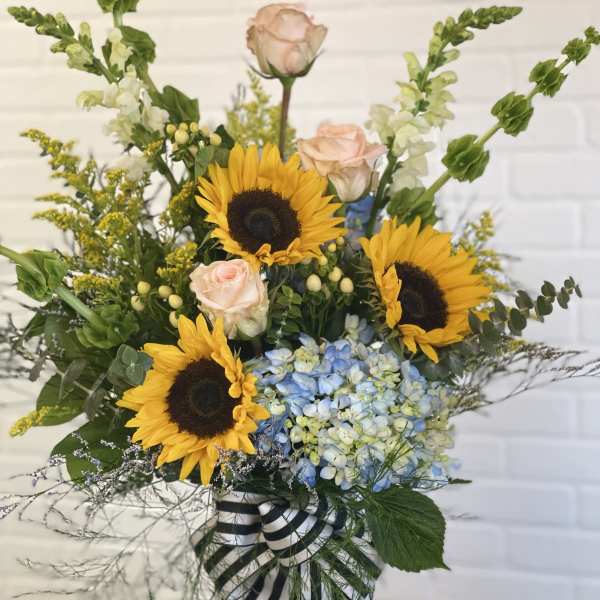 Sunflowers, pale roses, and blue hydrangeas in a striped ribbon vase