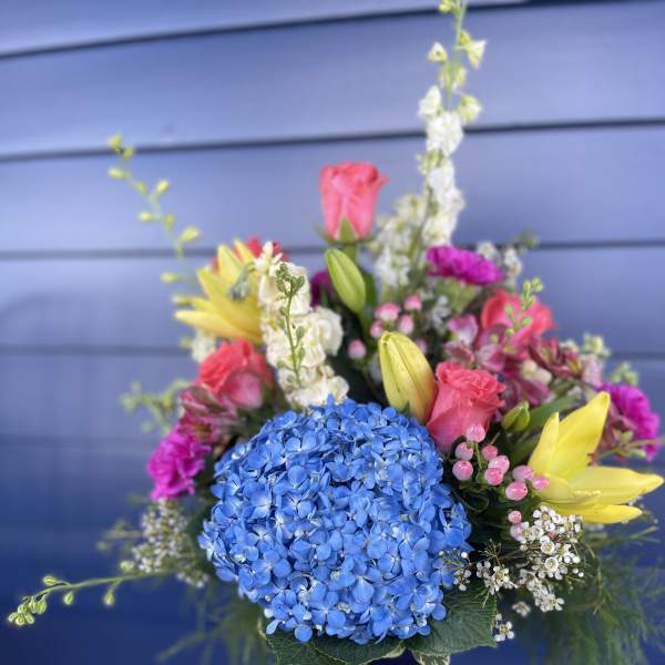Colorful mixed bouquet in a blue glass vase with hydrangea, lilies, and roses