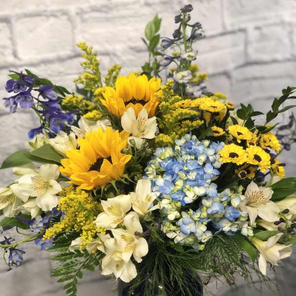 Mixed bouquet with sunflowers, blue hydrangeas, and white alstroemeria in a dark vase