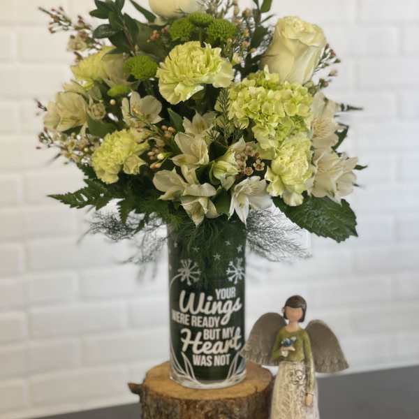 Cream and green floral arrangement in a decorated glass vase beside a small angel figurine.