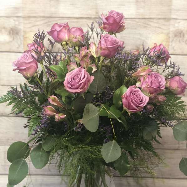 Pink roses in a clear glass vase with mixed greenery