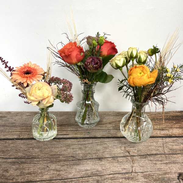 Three small flower arrangements in clear glass vases on a wooden surface