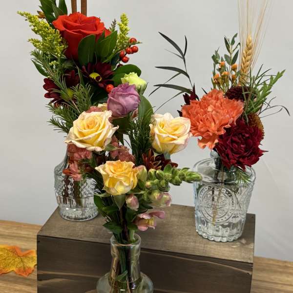 Three floral arrangements in glass vases with roses and carnations