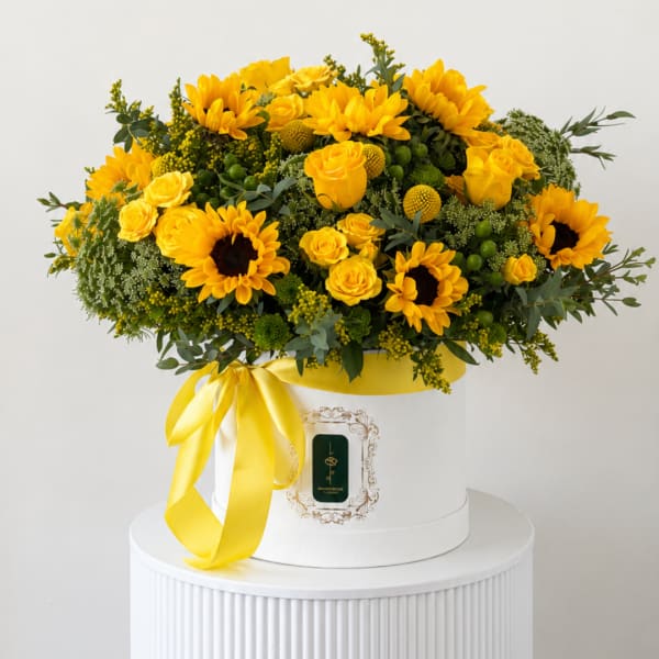 Yellow sunflowers and roses arranged in a white hat box with a yellow ribbon