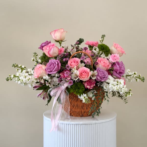 Pink and purple rose arrangement in a wicker basket with ribbon