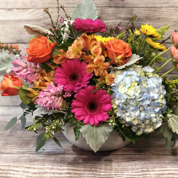 Mixed bouquet with roses, gerbera daisies, hydrangea, and orange blooms in a low vase