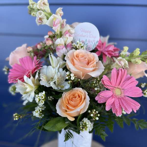 Pink and peach flower arrangement in a white vase with a Mother's Day card