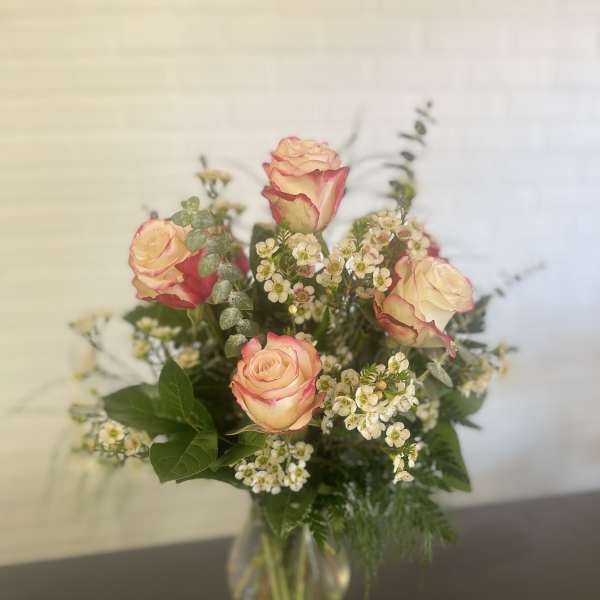 Pink-edged roses in a clear glass vase with small white filler flowers