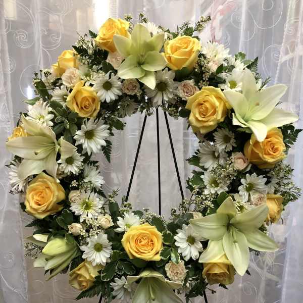Large floral wreath with yellow roses, white daisies, and pale lilies on a stand