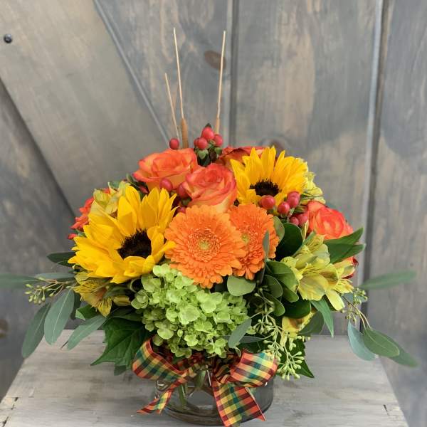 Bright mixed bouquet with sunflowers, orange roses, and gerbera daisies in a glass vase