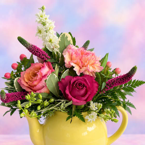 Pink and peach flowers arranged in a yellow teapot vase