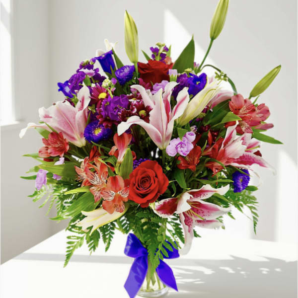 Mixed bouquet of lilies, roses, and purple flowers in a glass vase