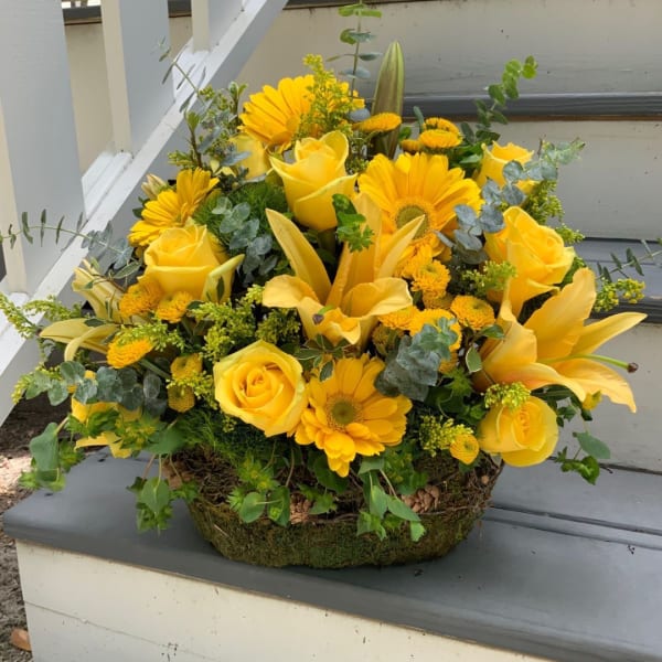 Yellow roses and gerbera daisies arranged in a low basket