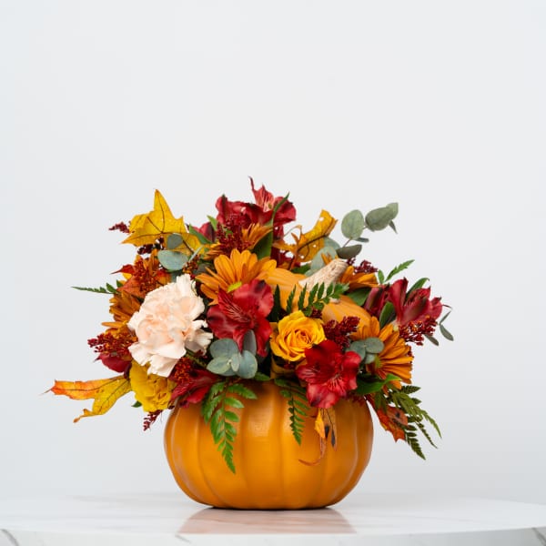 Autumn flower arrangement in a pumpkin-shaped container with red, orange, and cream blooms