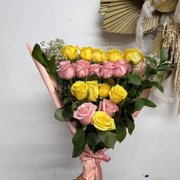 Bouquet of yellow and pink roses wrapped in pink paper with a satin ribbon