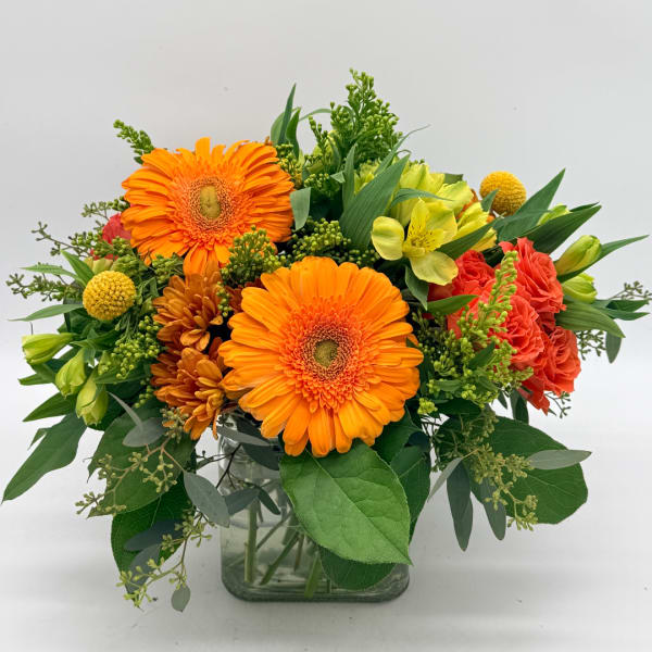Bright mixed flower arrangement in a clear glass vase with orange gerberas and coral blooms