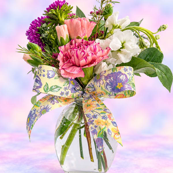 Mixed pink, white, and purple bouquet in a clear glass vase with a floral ribbon