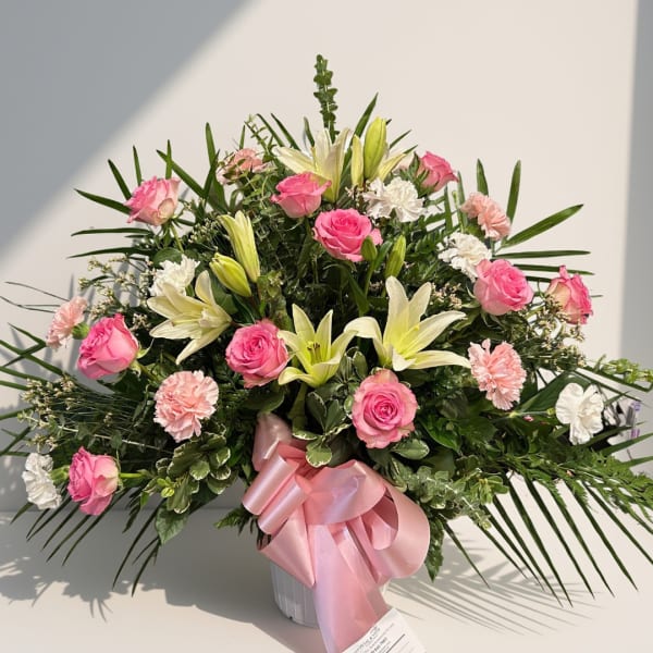 Pink roses and white lilies in a vase with a pink ribbon