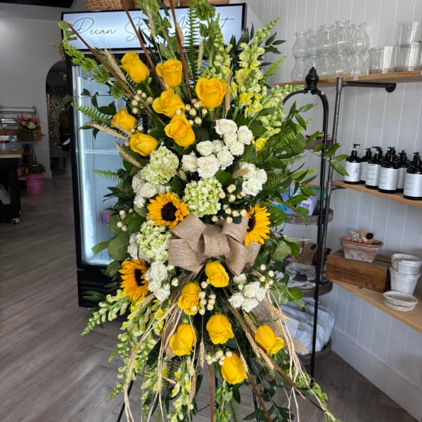 Tall floral standing spray with yellow and white roses, sunflowers, and a burlap bow