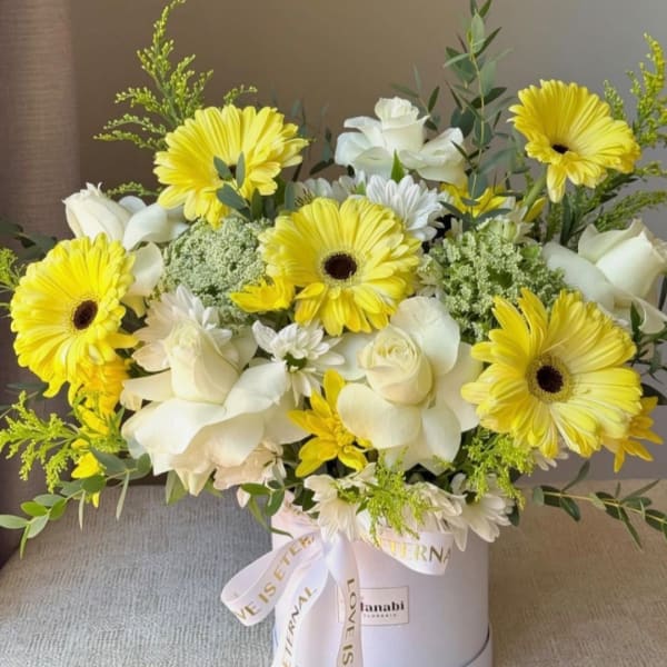 Yellow gerbera daisies and white roses in a white hat box