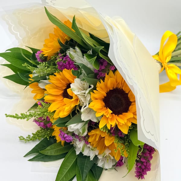 Bouquet of sunflowers and white flowers wrapped in cream paper with a yellow ribbon