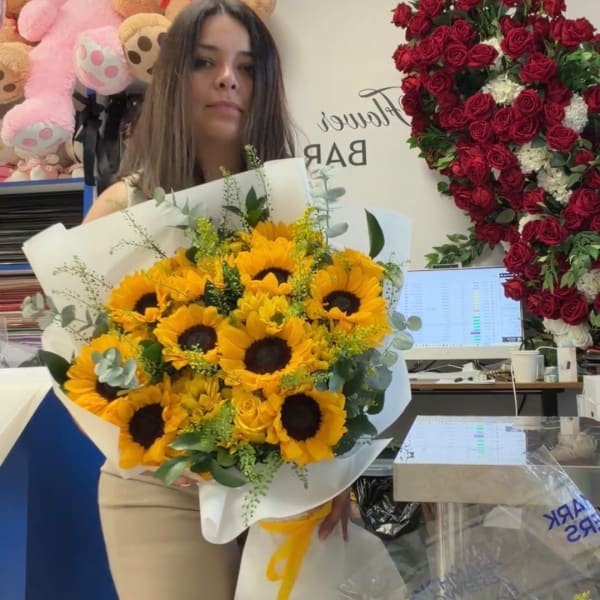 Woman holding a bouquet of sunflowers and yellow roses wrapped in white paper
