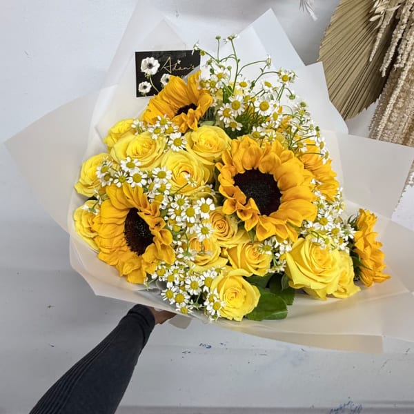 Bouquet of yellow roses, sunflowers, and small white daisies wrapped in white paper