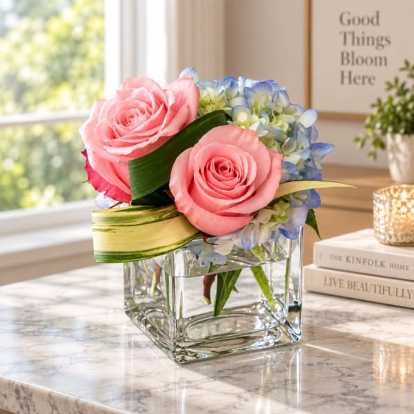 Pink roses and blue hydrangeas in a clear square vase