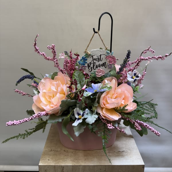 Peach floral arrangement in a pink container with a hanging "Just Bloom" sign