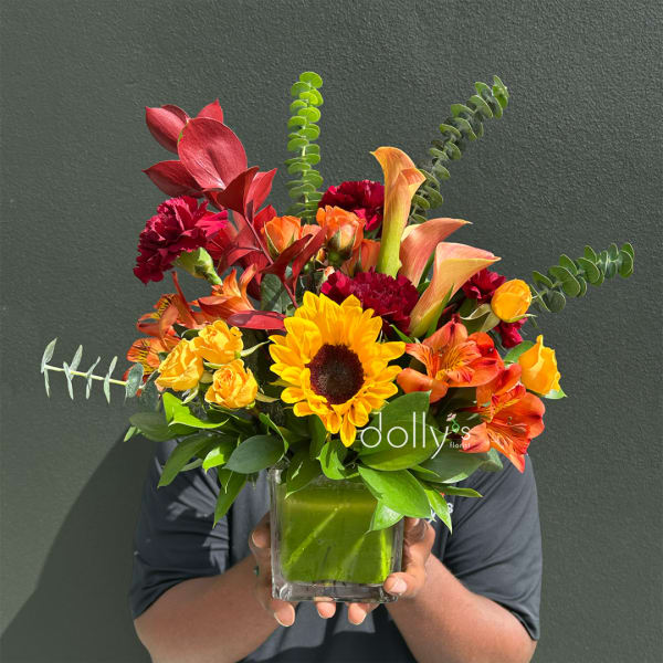 Bright mixed bouquet in a square glass vase with sunflowers, calla lilies, and carnations