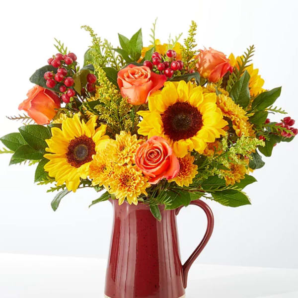 Sunflower and orange rose bouquet in a red pitcher vase