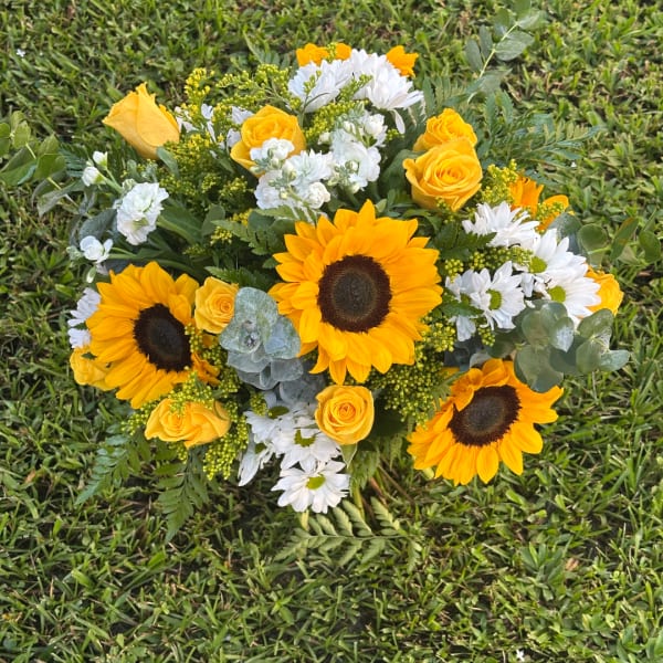 Bouquet of sunflowers, yellow roses, and white daisies on grass