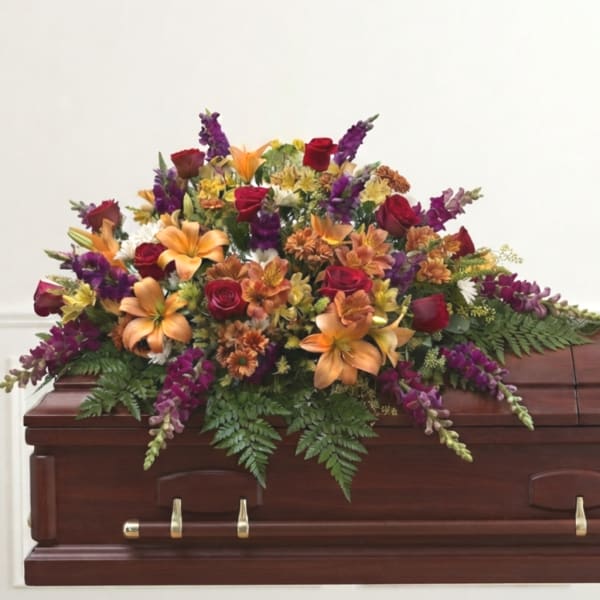 Colorful floral spray on a wooden casket with roses and lilies