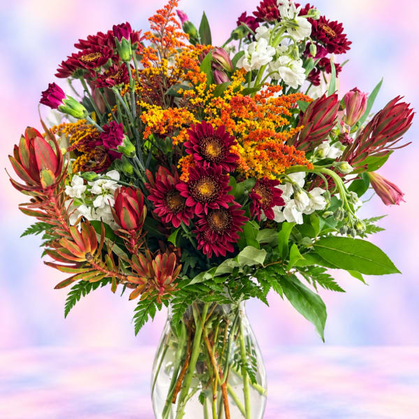 Mixed bouquet of burgundy, orange, and white flowers in a clear glass vase