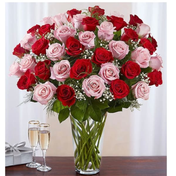 Red and pink roses in a clear glass vase with two champagne flutes