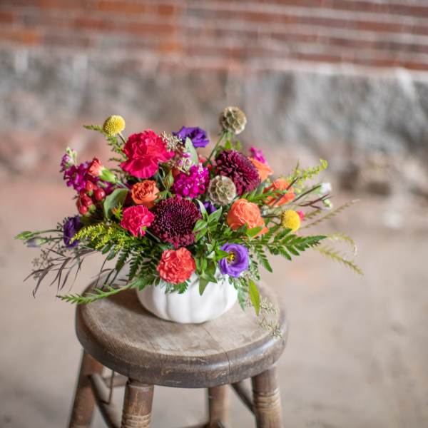 Colorful mixed bouquet in a white pumpkin-shaped vase on a wooden stool