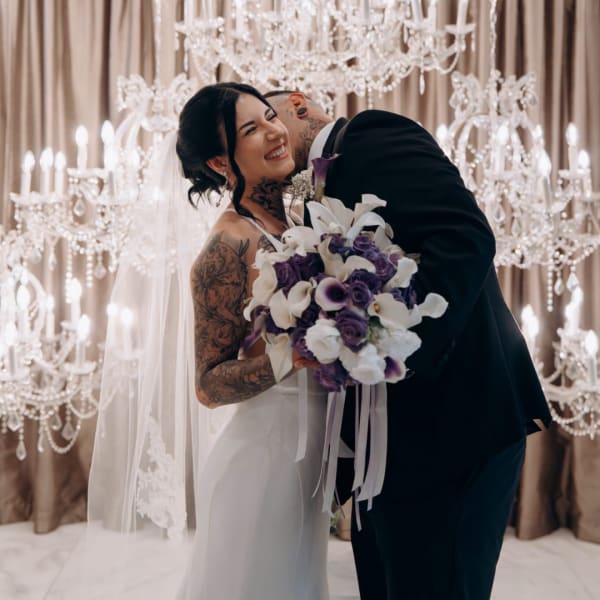 Bride holding a white and purple wedding bouquet while embracing a groom