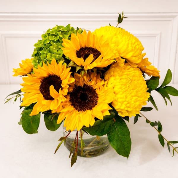 Yellow sunflowers and mums arranged in a clear glass vase