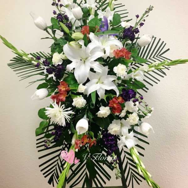 Tall funeral spray with white lilies, purple accents, and palm fronds