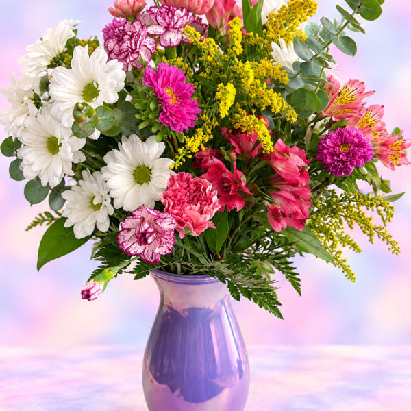Mixed bouquet of daisies, carnations, and pink blooms in a purple vase