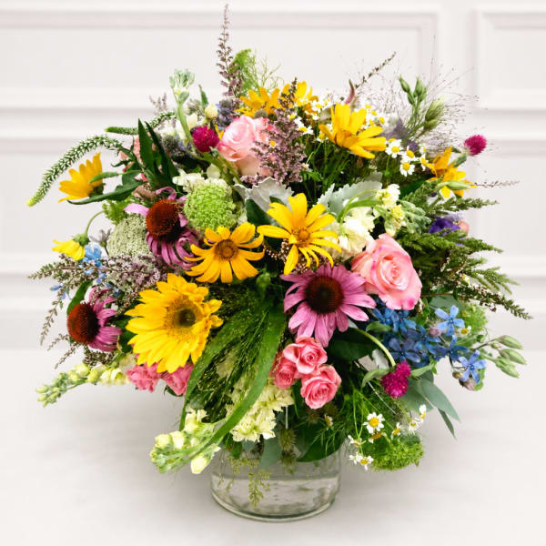 Mixed bouquet of yellow, pink, purple, and white flowers in a clear glass vase