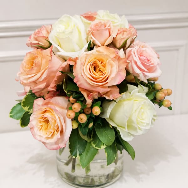 Peach and white roses arranged in a clear glass vase
