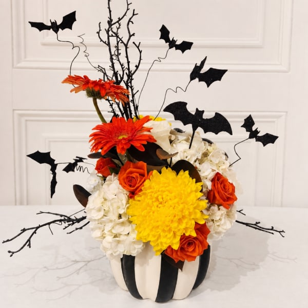 Halloween floral arrangement in a striped pumpkin container with bats and orange blooms