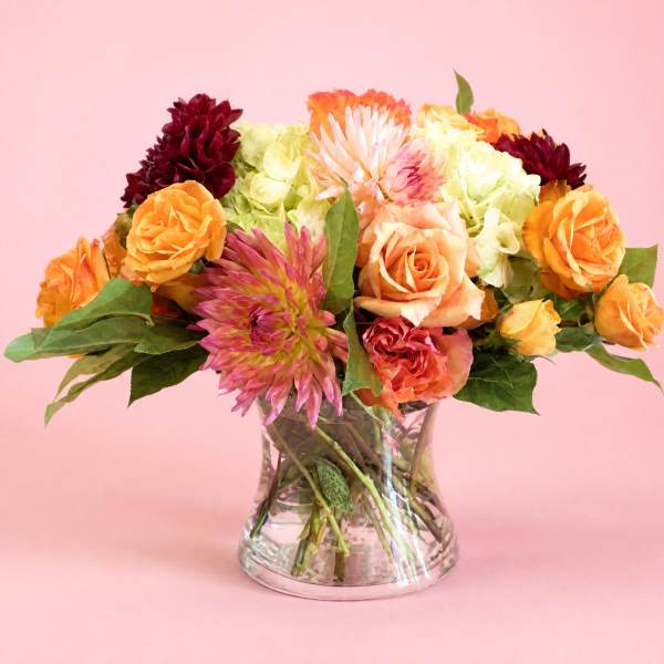Mixed bouquet of orange, pink, and burgundy flowers in a clear glass vase