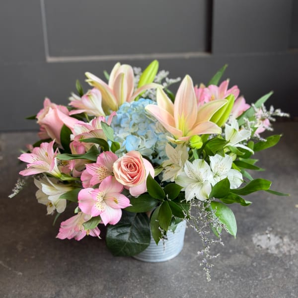 Pink and white bouquet with lilies, roses, and blue hydrangea in a white vase