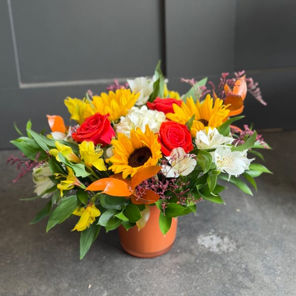 Colorful bouquet of sunflowers, roses, and white blooms in an orange vase
